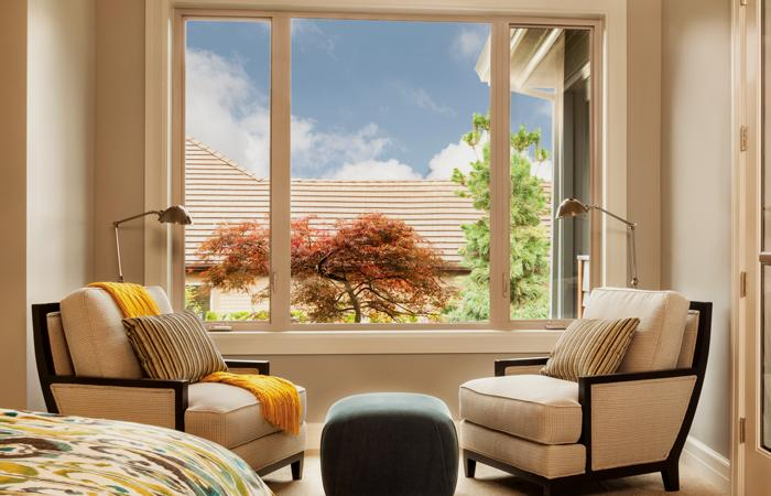 A bedroom with two chairs and an ottoman in front of a large window.