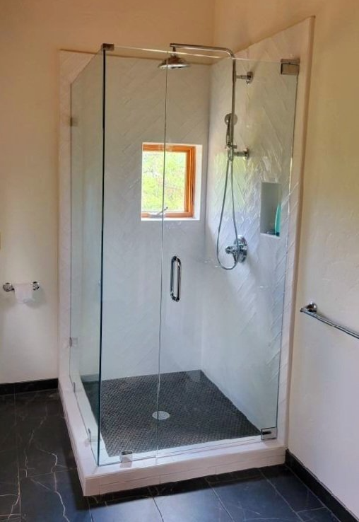 A bathroom with a walk in shower with a glass door and a window.