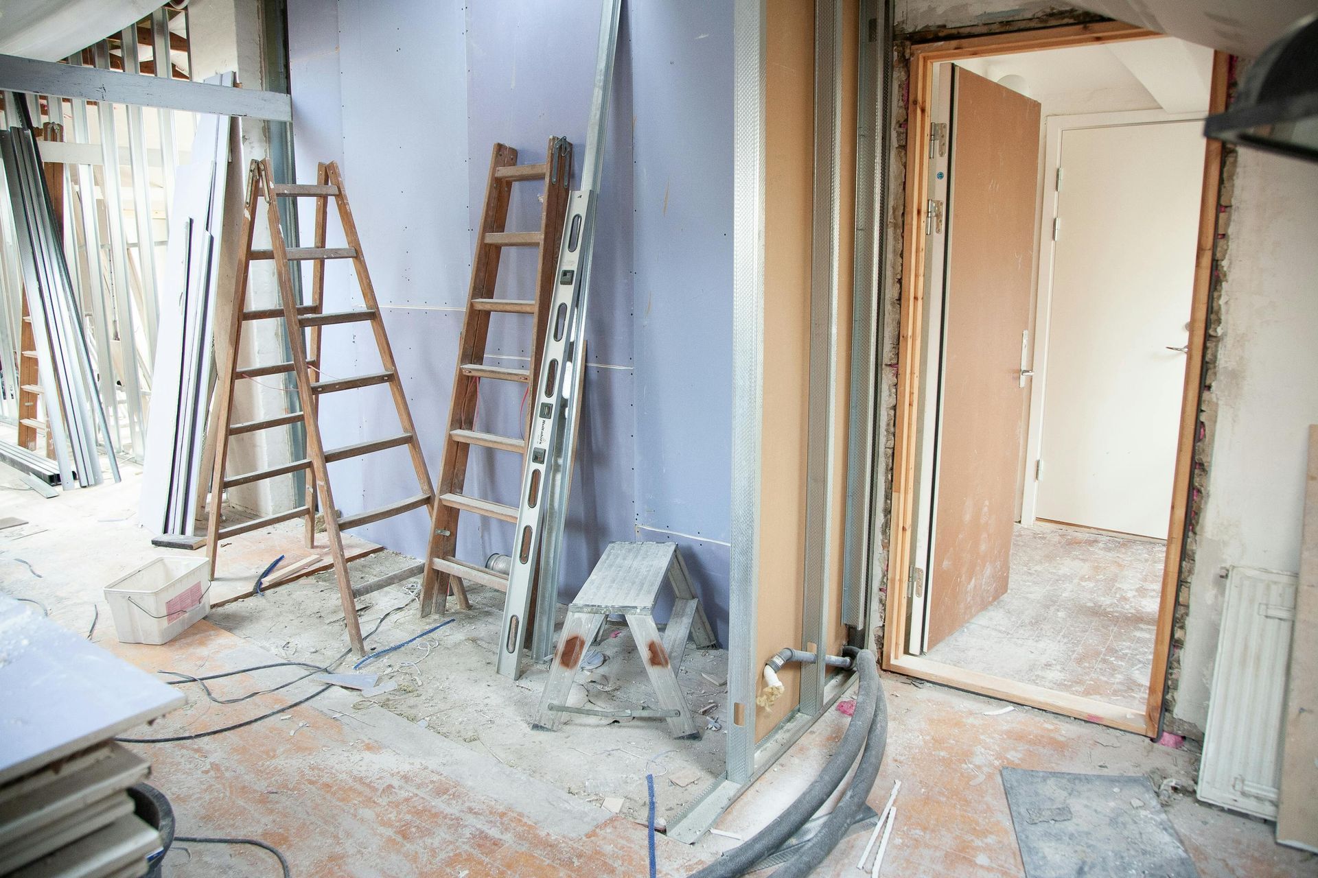 Interior renovation with ladders, exposed framing, and unfinished walls in a dusty room