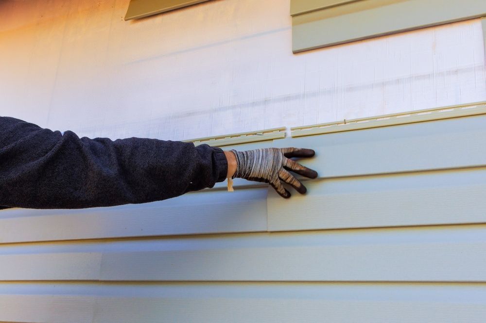 Gloved hand reaching toward white horizontal siding on a house exterior