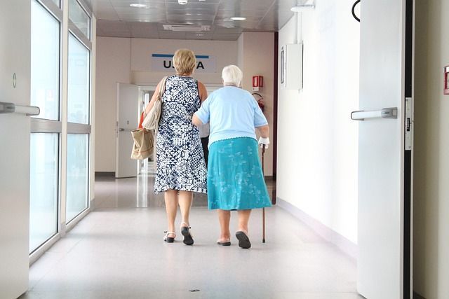 The backs of a lady and a senior female walking in a hospital corridor.