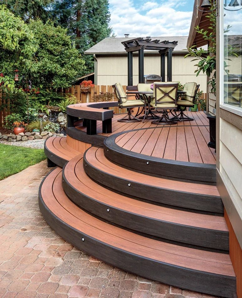 Curved wooden deck with steps, seating area, and pergola in a backyard.
