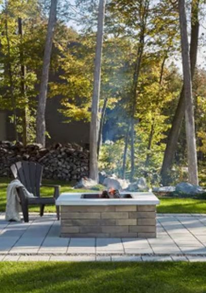 Fire pit with burning flames, surrounded by a brick base and outdoor seating in a wooded area.