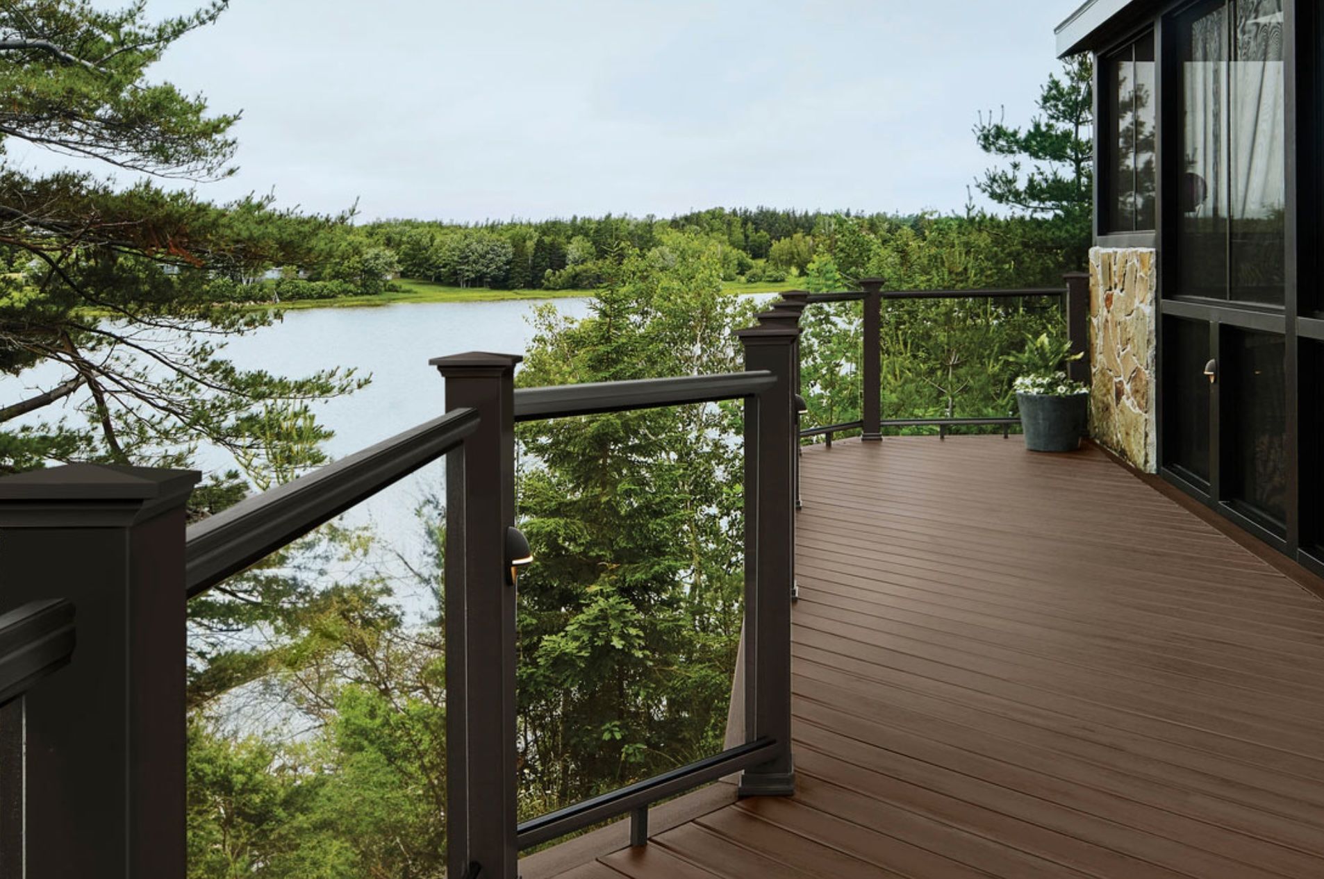 Deck overlooking lake, with brown railings and composite decking; view of trees and water.