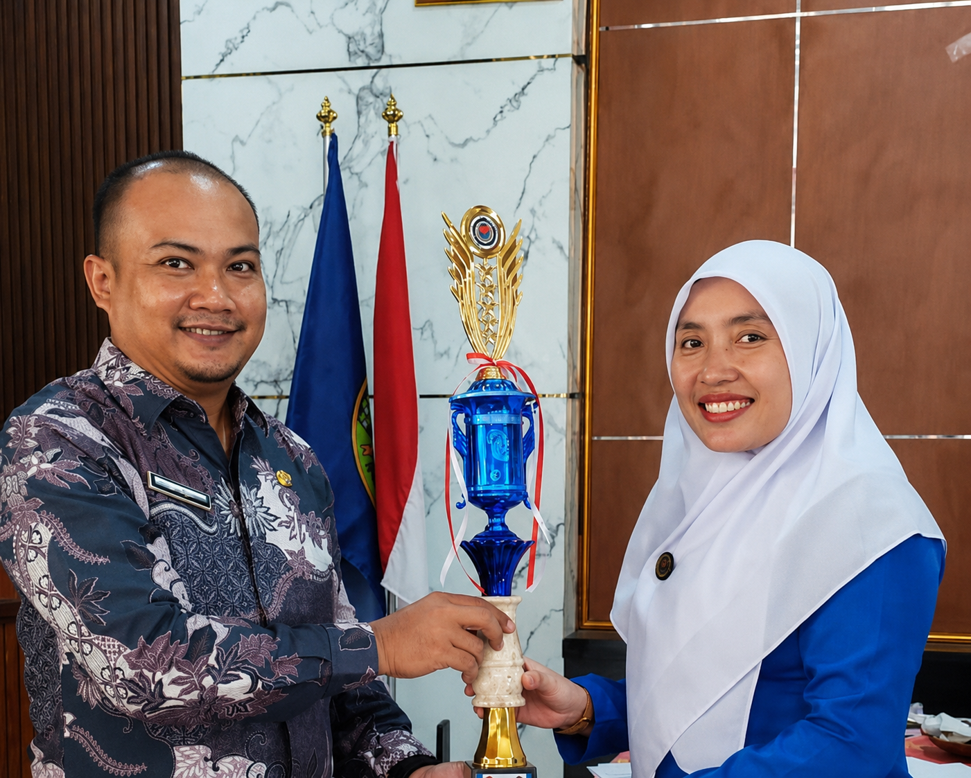 Two people holding a trophy in front of flags, smiling indoors.