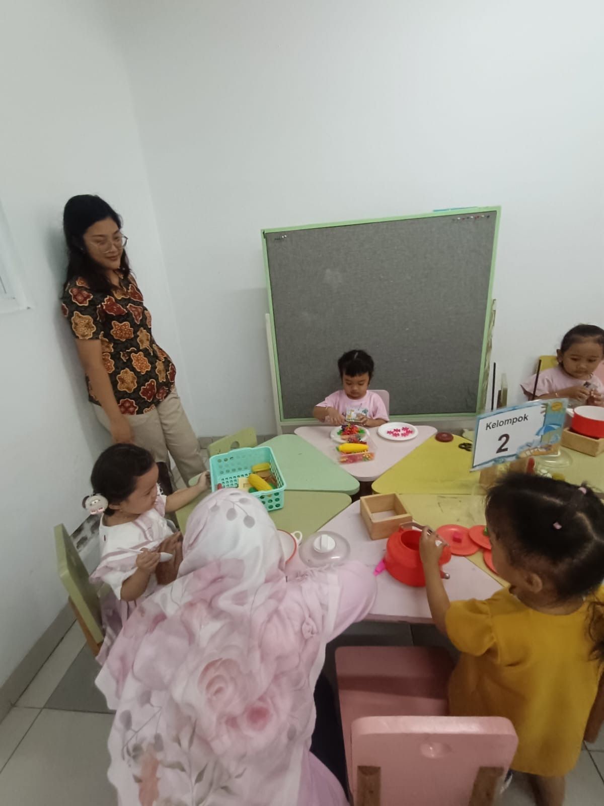 Children balancing on a wooden track in an indoor play area. Red carpet, other kids & adults watching.