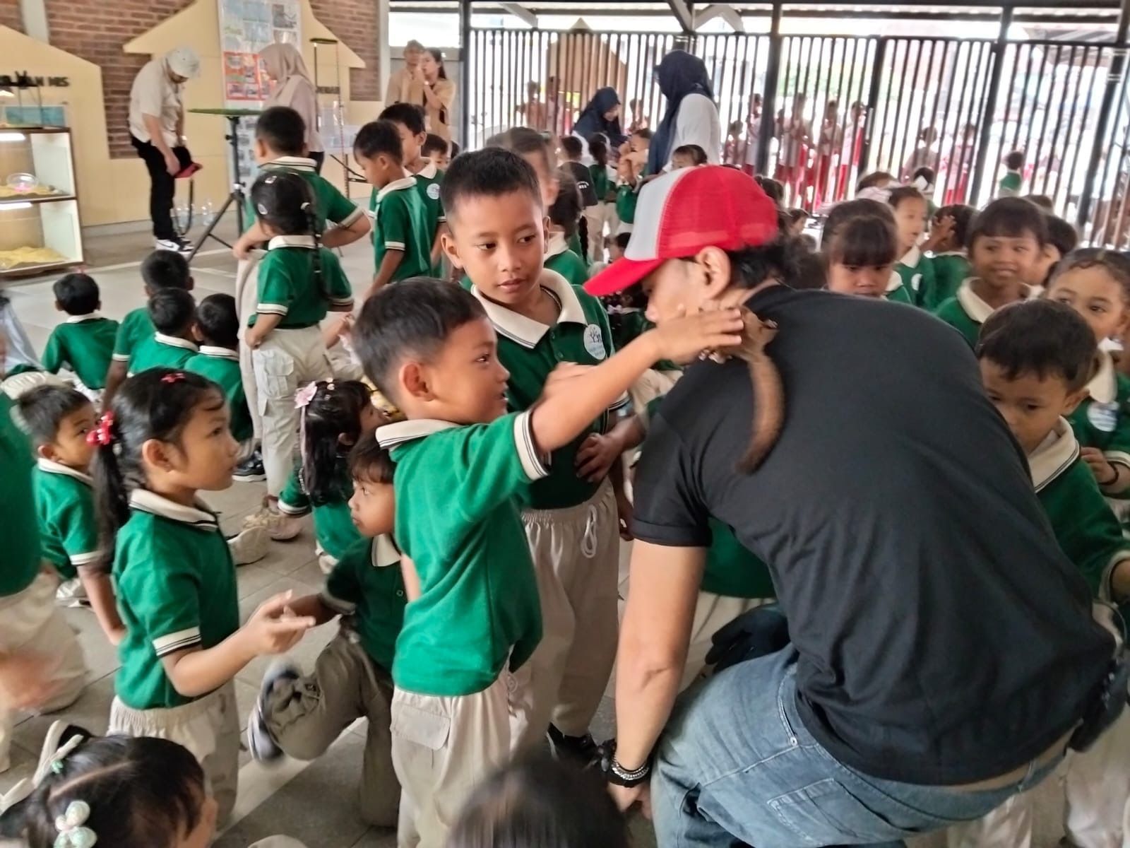 Children balancing on a wooden track in an indoor play area. Red carpet, other kids & adults watching.