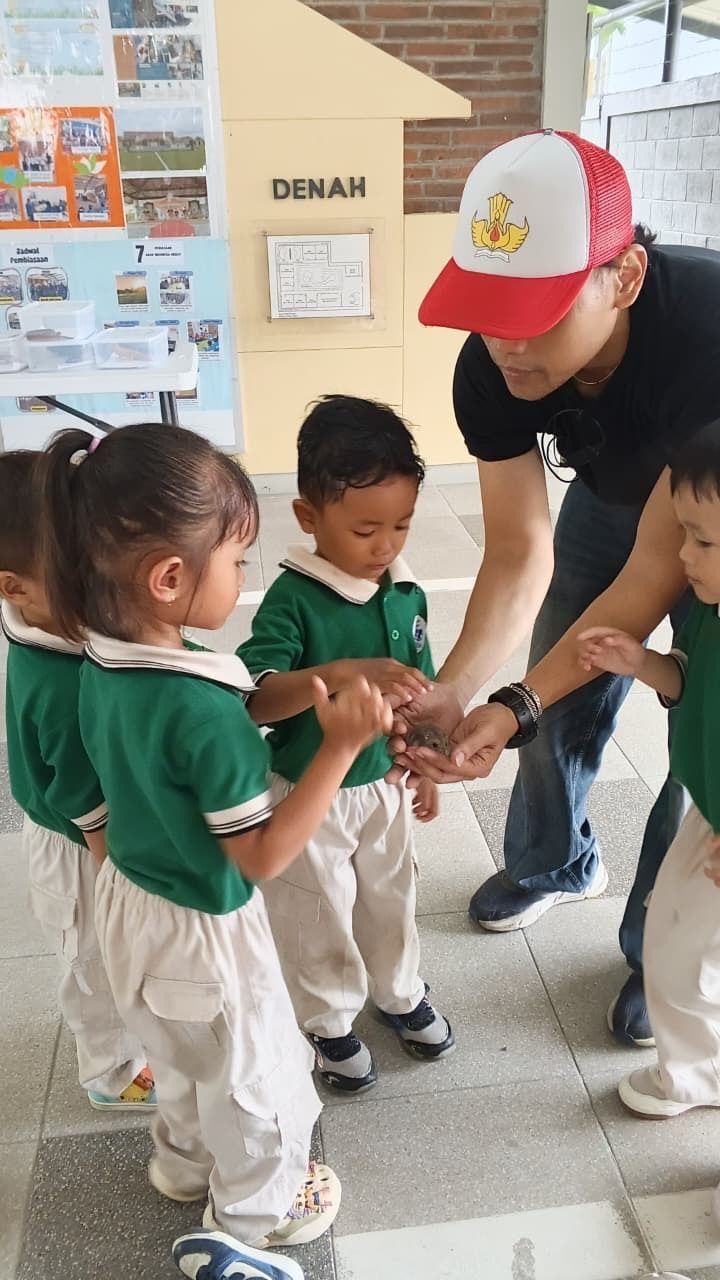 Children in green shirts and tan pants line up on red carpet. Indoor event.