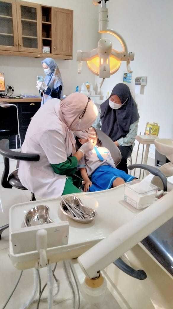 Dentist examining a child's teeth in a clinic. Two assistants are present.