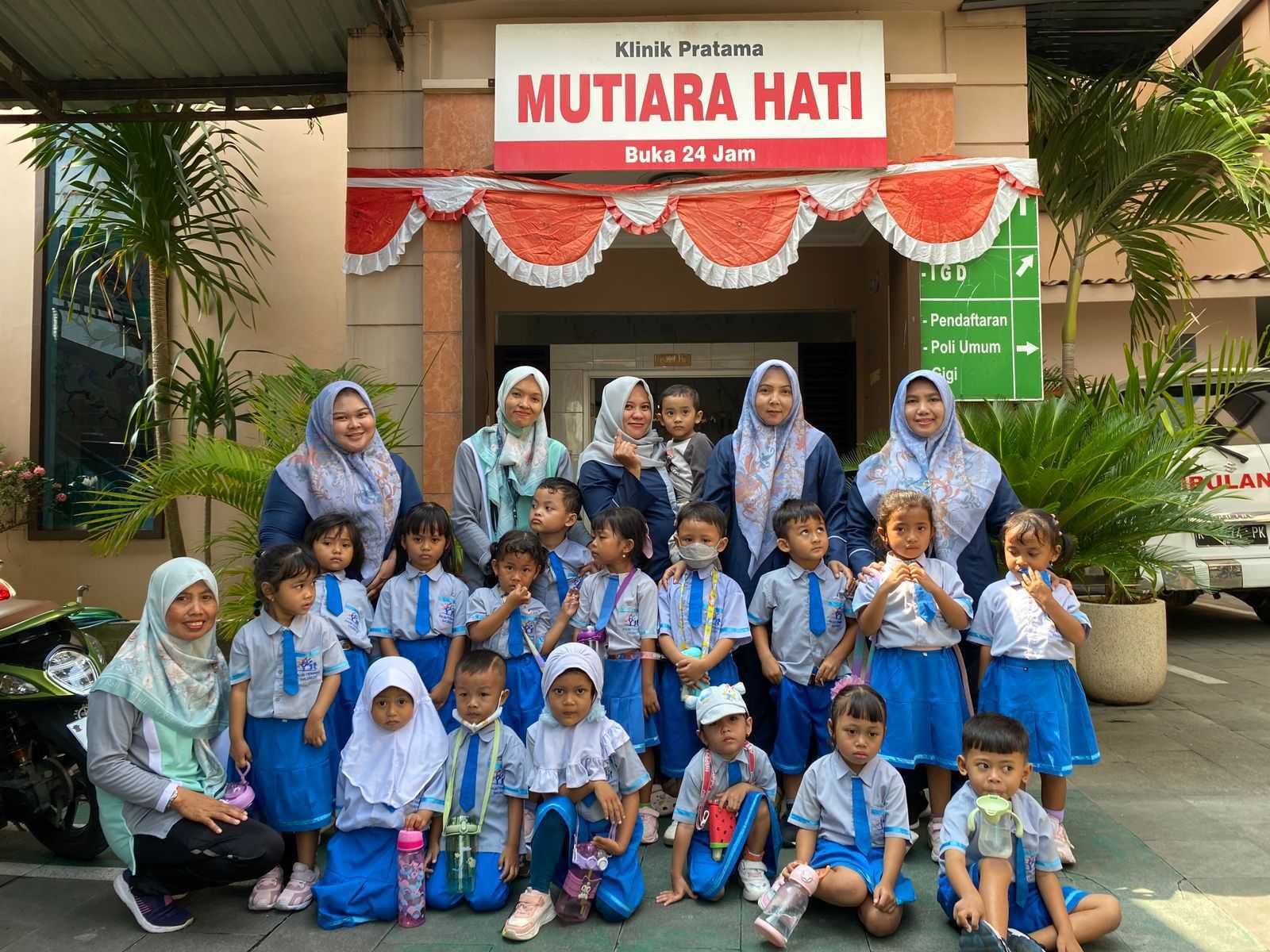 Children in school uniforms pose with adults outside a clinic,