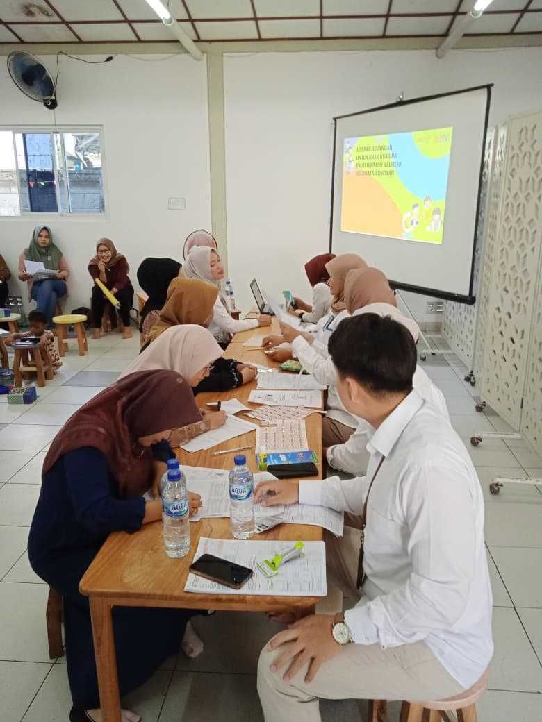 People in a meeting at a table, watching a presentation on a screen.