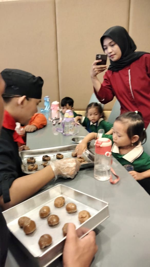Children in green shirts at a table, making cookies with an instructor in a chef's uniform.