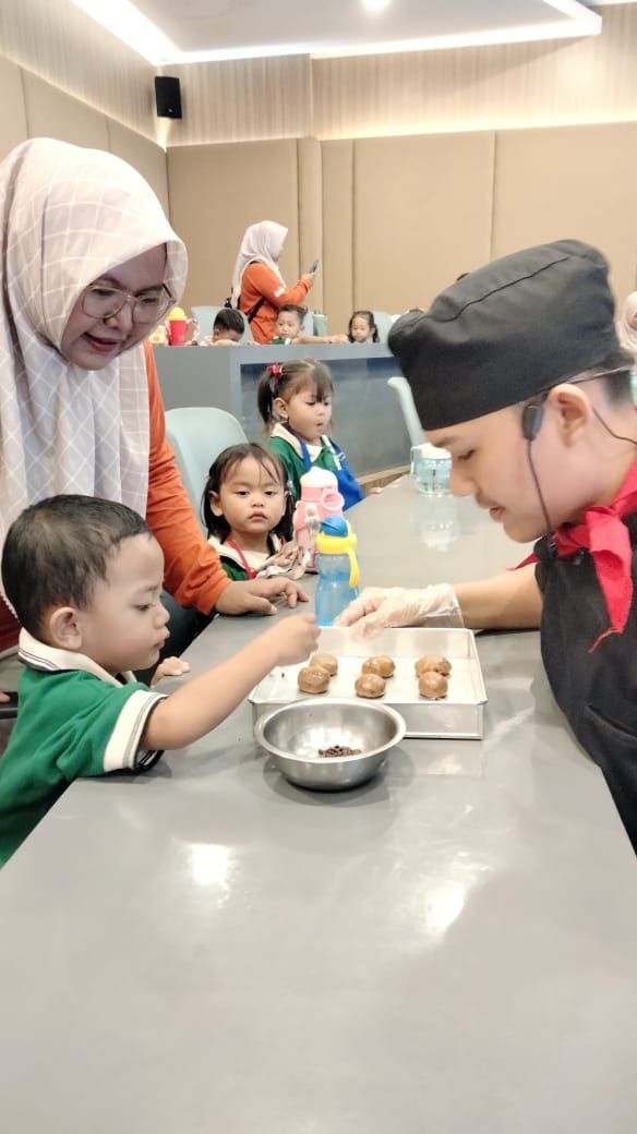 A chef assisting a child decorate treats. Other children and an adult woman watch.