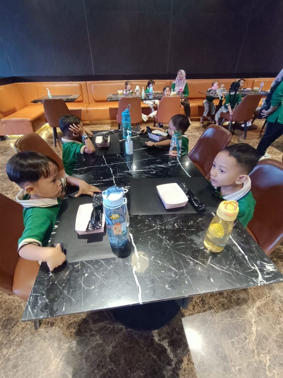 Children in green shirts sitting at a marble table in a restaurant.