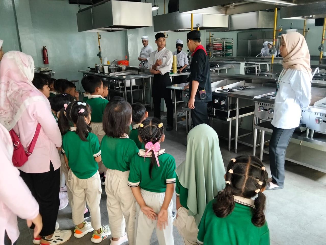 Children in green shirts on a kitchen tour, chefs demonstrate.