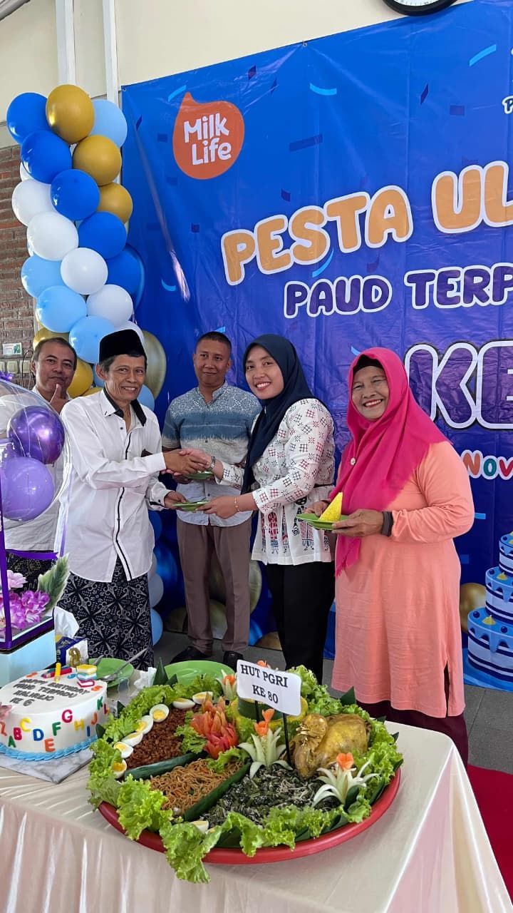 People at a celebration; they are holding food, in front of a banner and balloons.