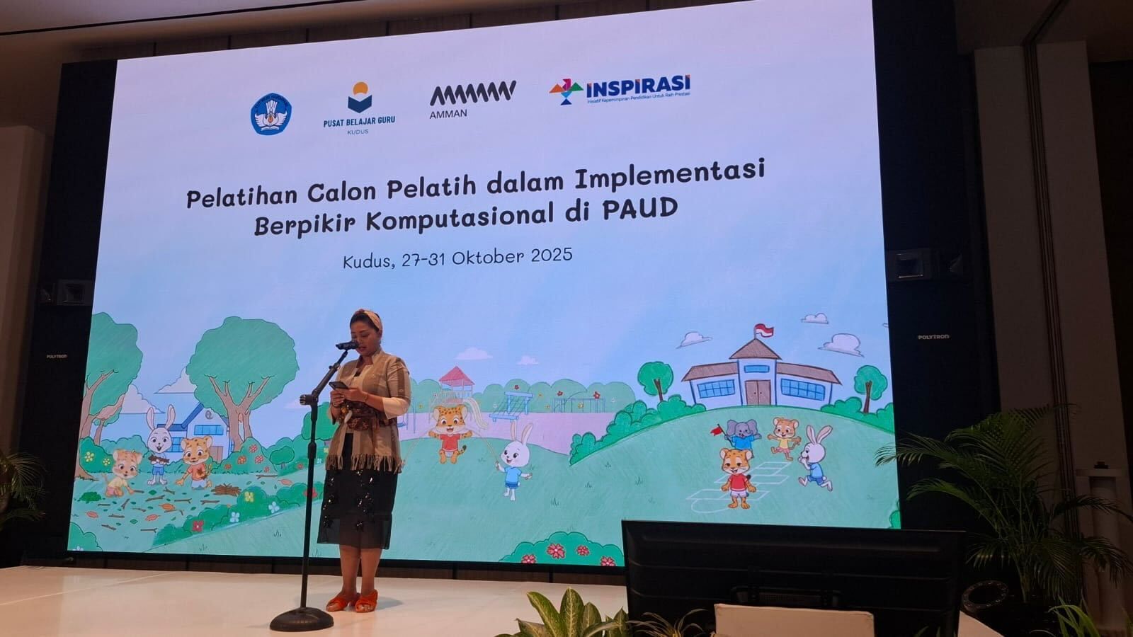 Woman speaking at a presentation on computational thinking in early childhood education, with a large screen behind her.