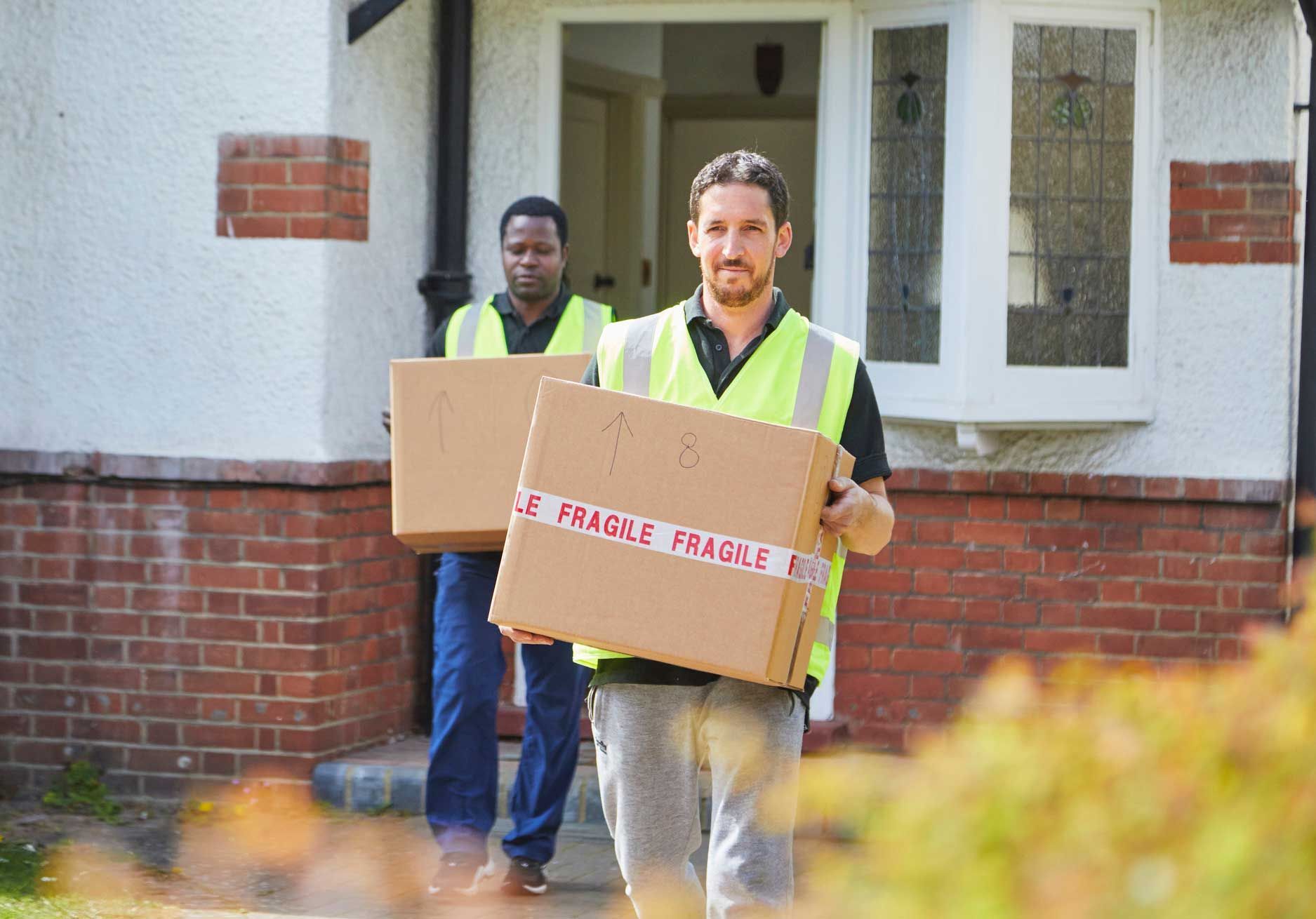 Two removal men are carrying boxes, and one of them is smiling