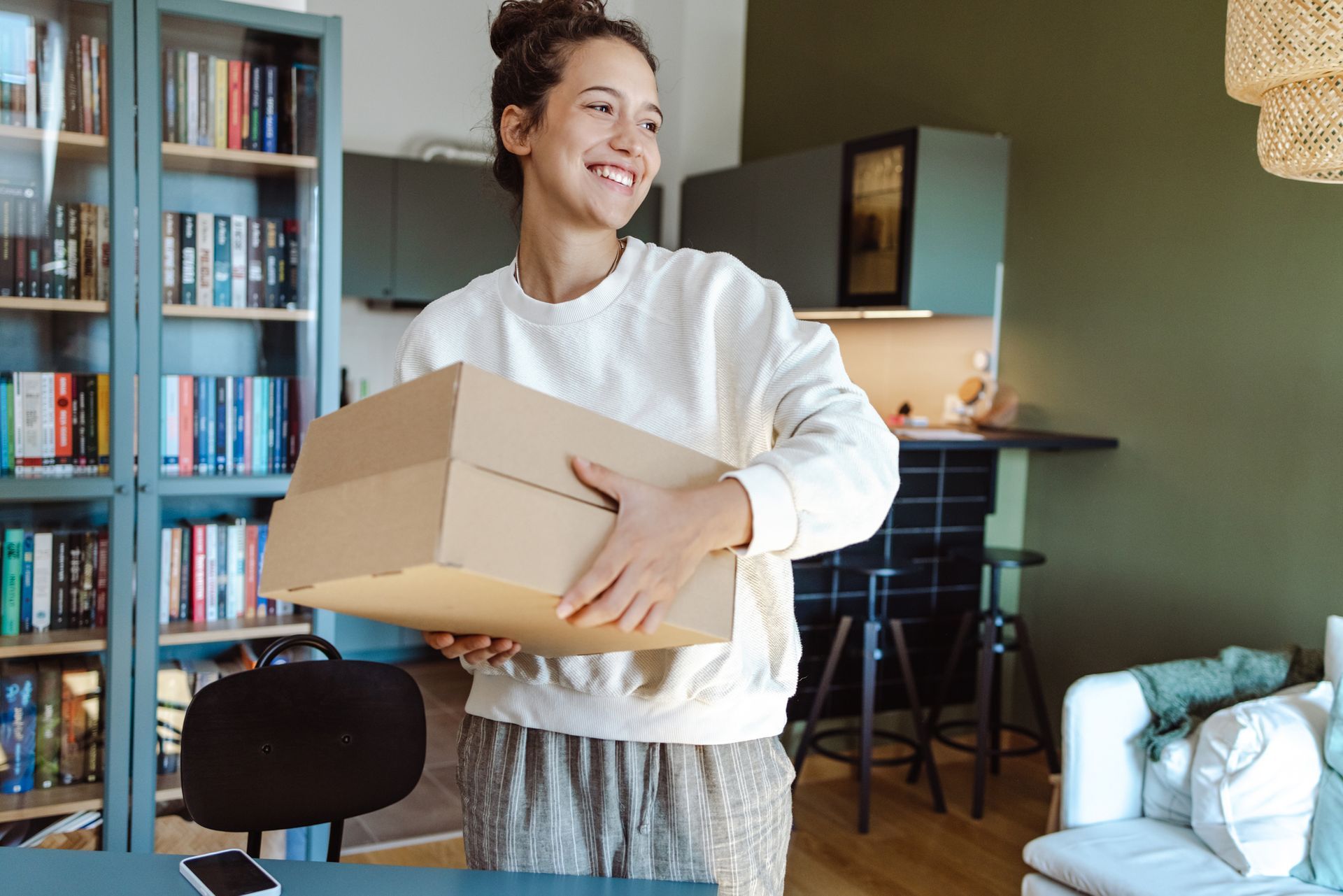 Smiling young woman with cardboard boxes brought by her local mover company to her new home.