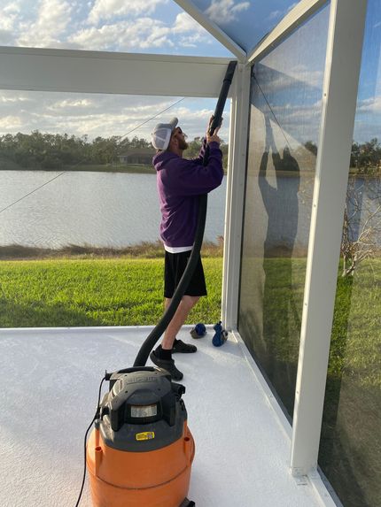 A man is cleaning a screened in porch with a vacuum cleaner.