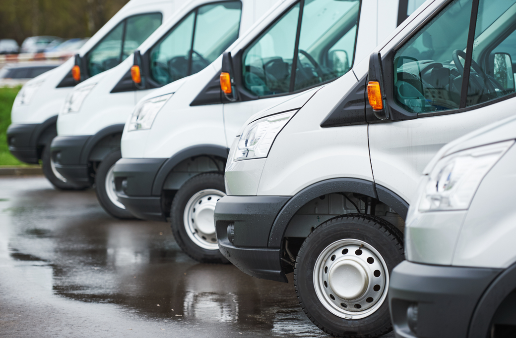 Line of white vans parked on a wet asphalt surface.