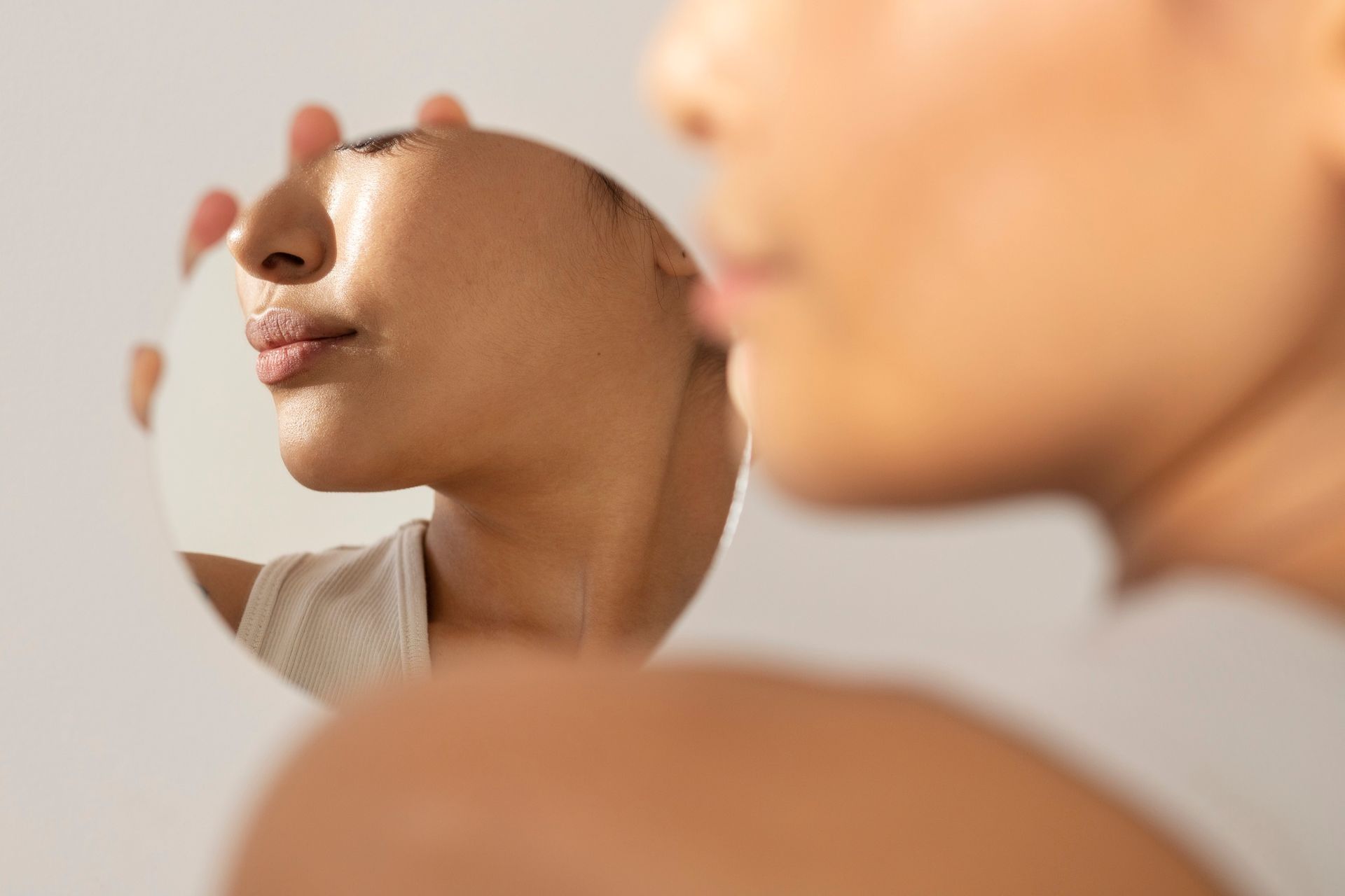 A woman is looking at her face in a mirror.