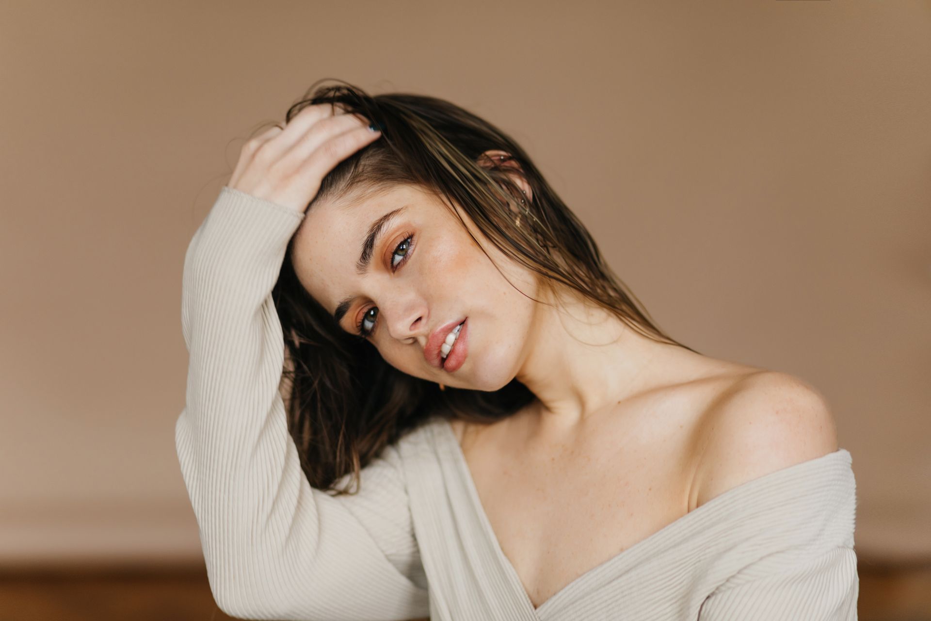 A woman in a white sweater is touching her hair.