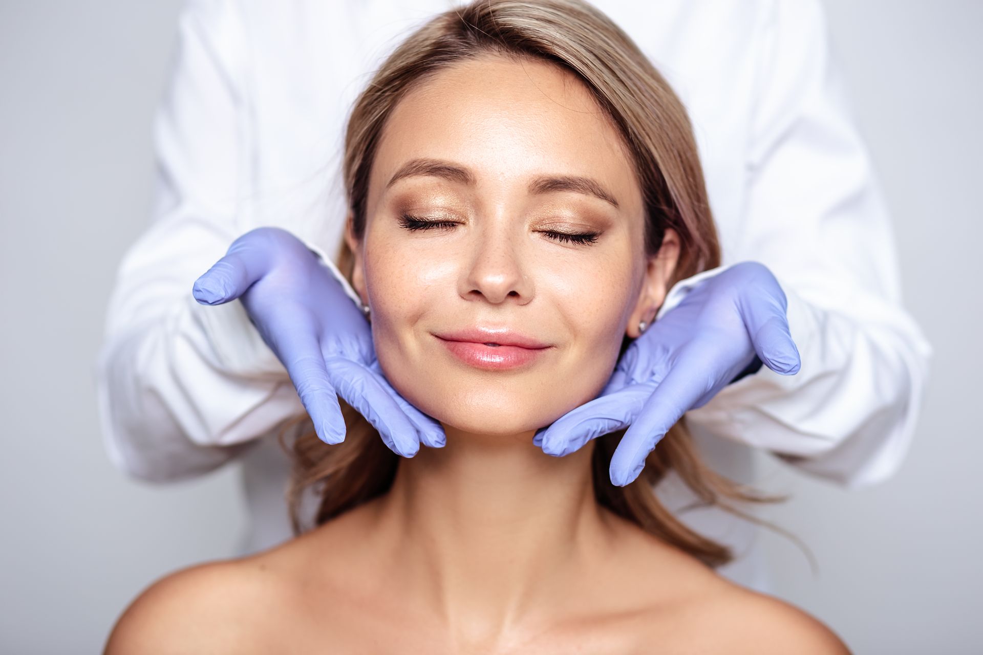 A woman is getting her face examined by a doctor wearing gloves.