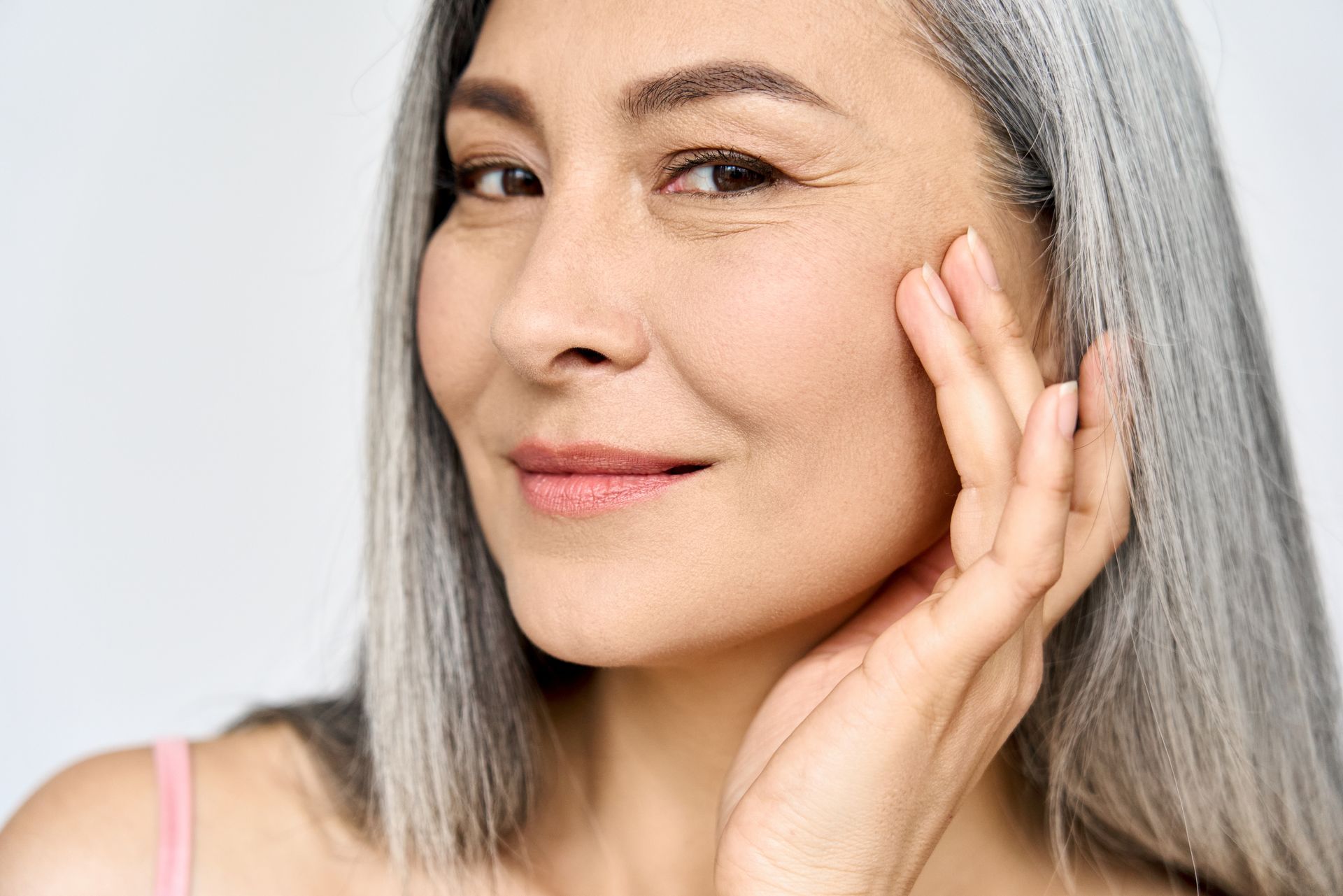 A close up of a woman with gray hair touching her face.