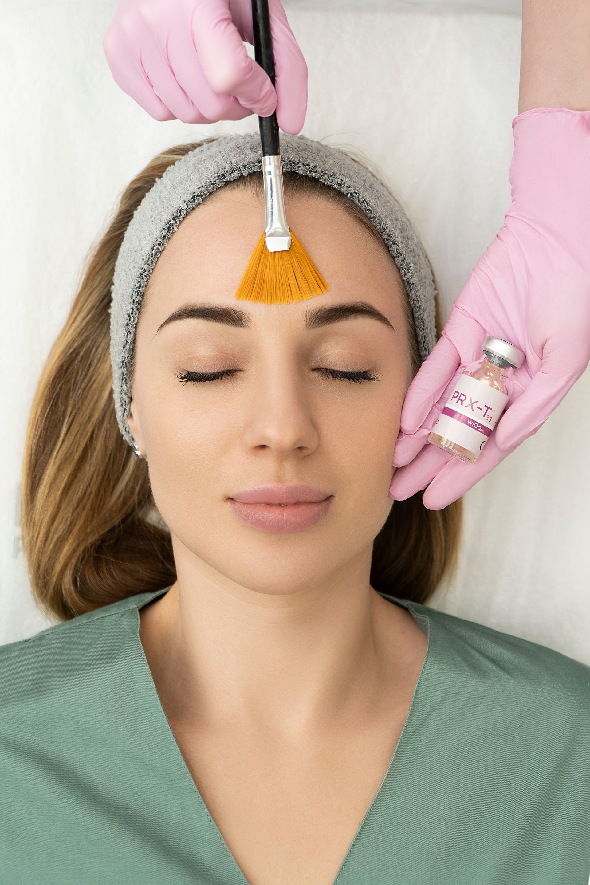 A woman is getting a facial treatment with a brush on her forehead.