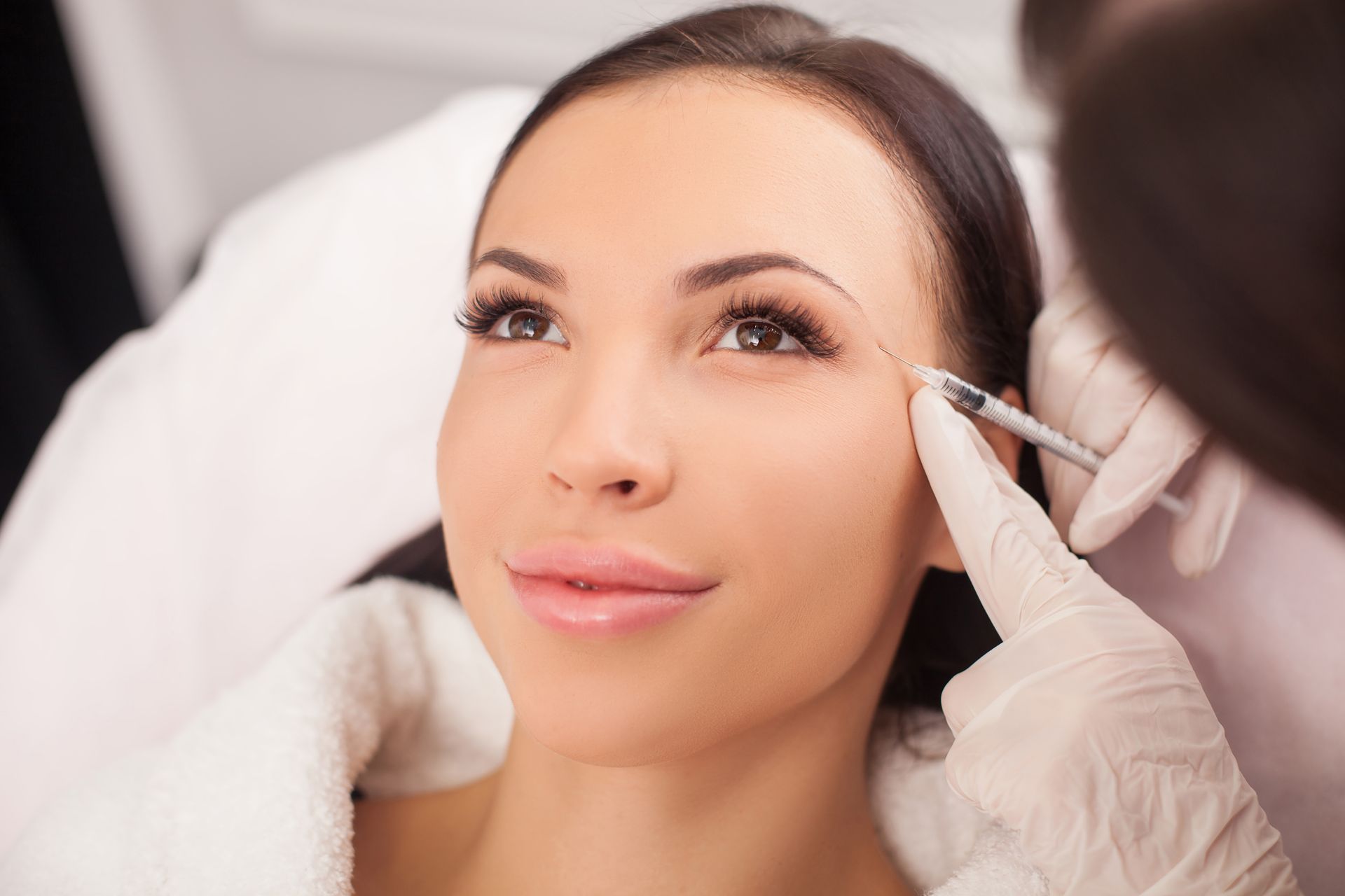 A woman is getting a botox injection in her forehead.