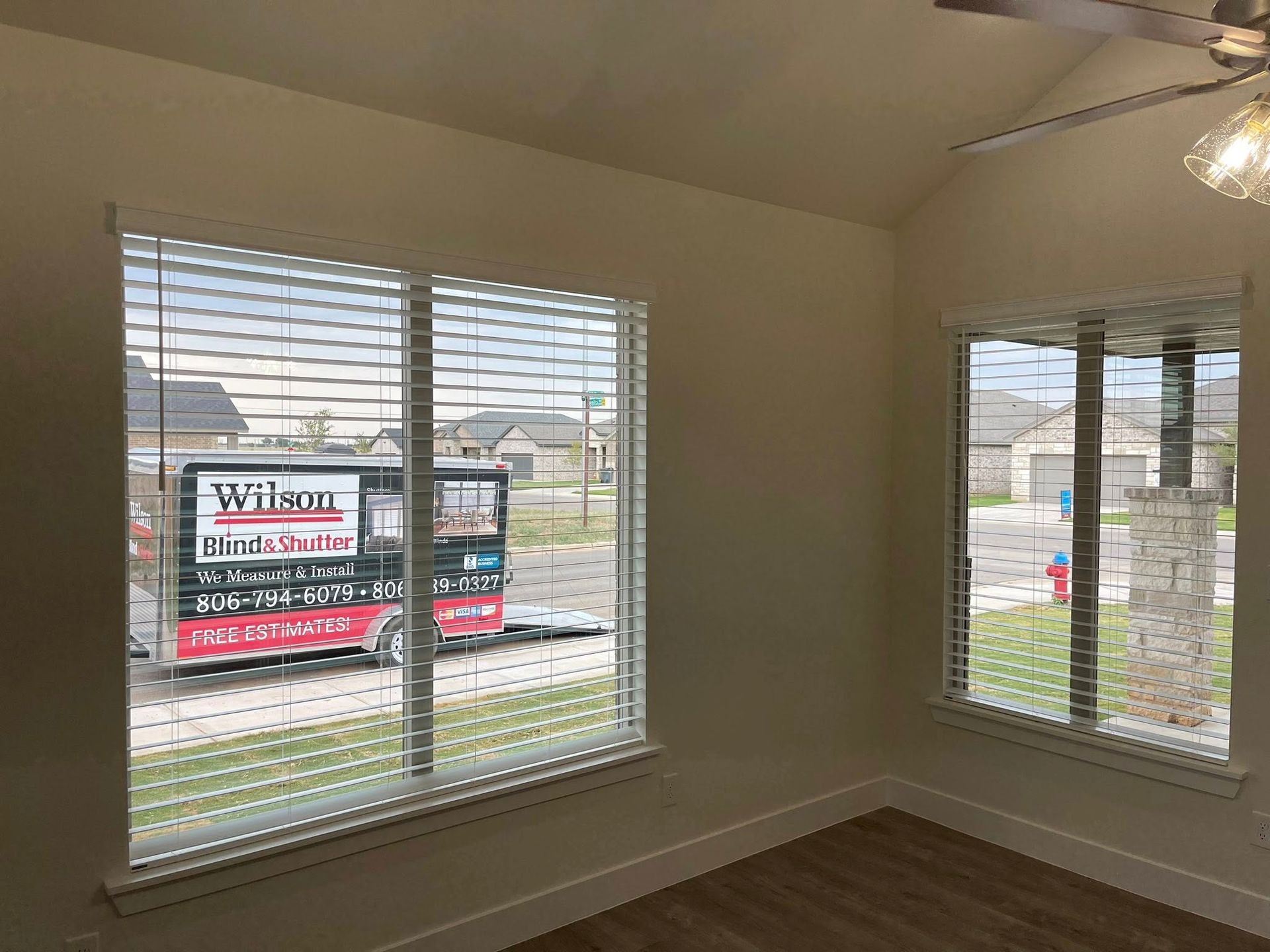 A bright room with light walls and wood floors, featuring windows that look out onto a street with a service trailer.