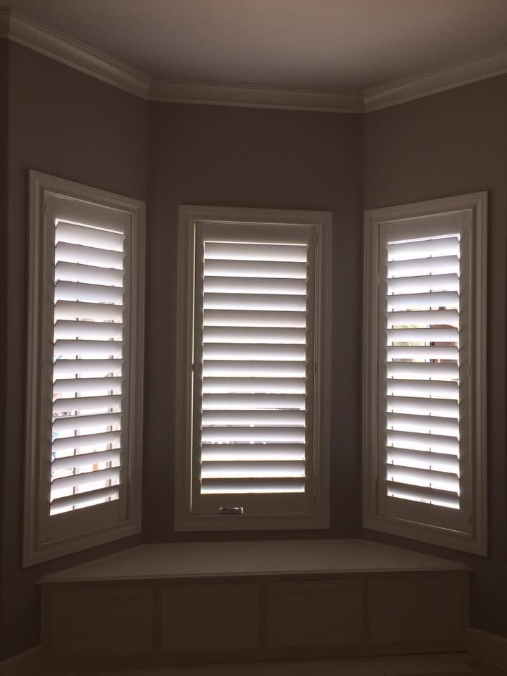 A bay window area with three white shutters and a built-in window seat underneath.