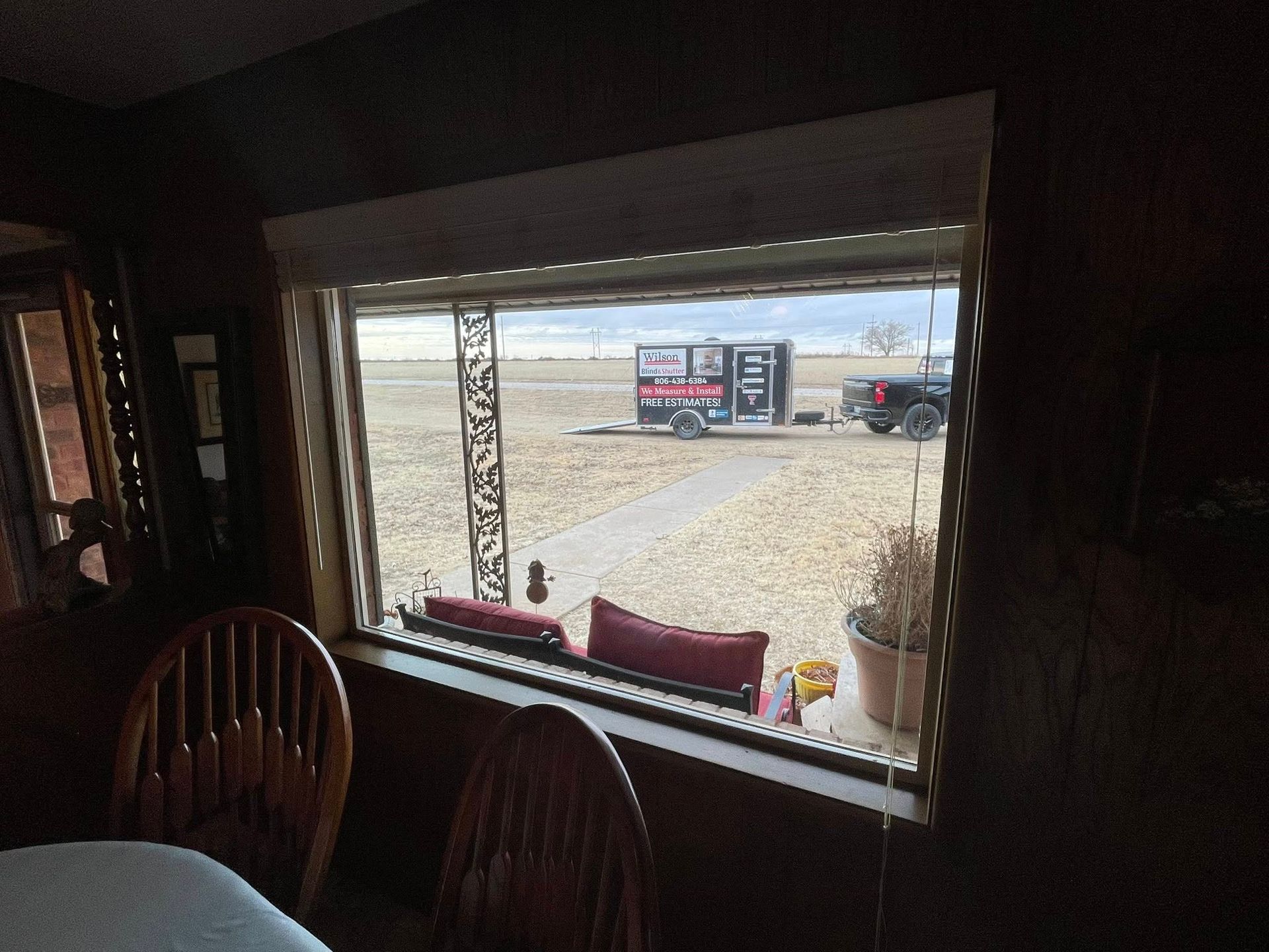 A view through a large window showing a trailer parked on a flat, dry landscape with a path leading to it.