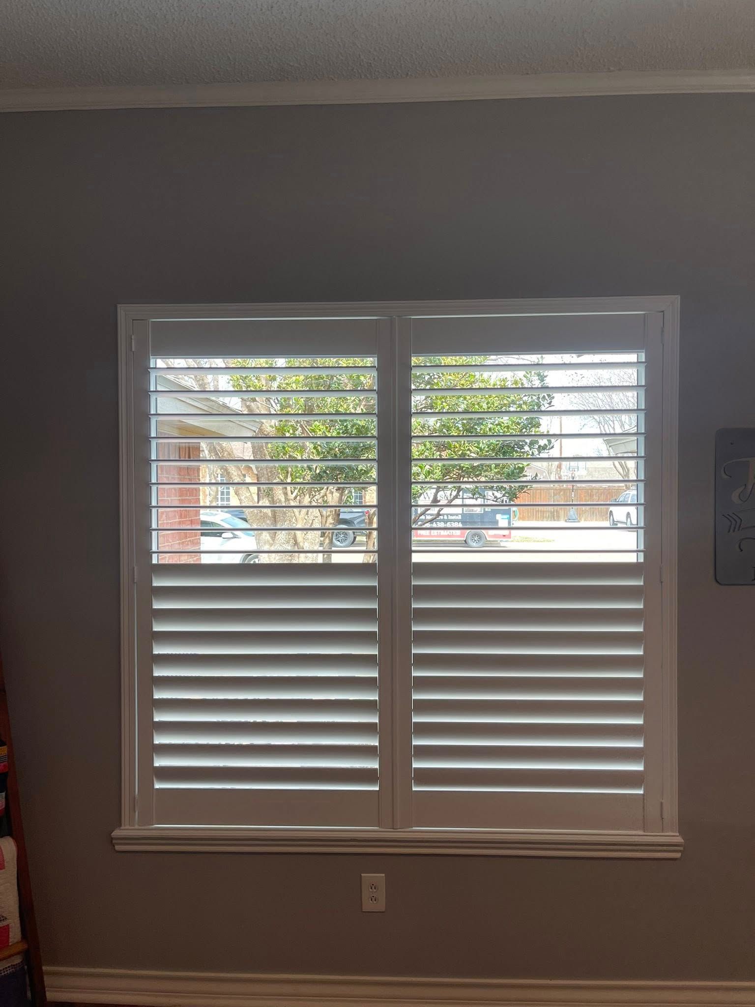 White plantation shutters installed on a window in a room with grey walls.
