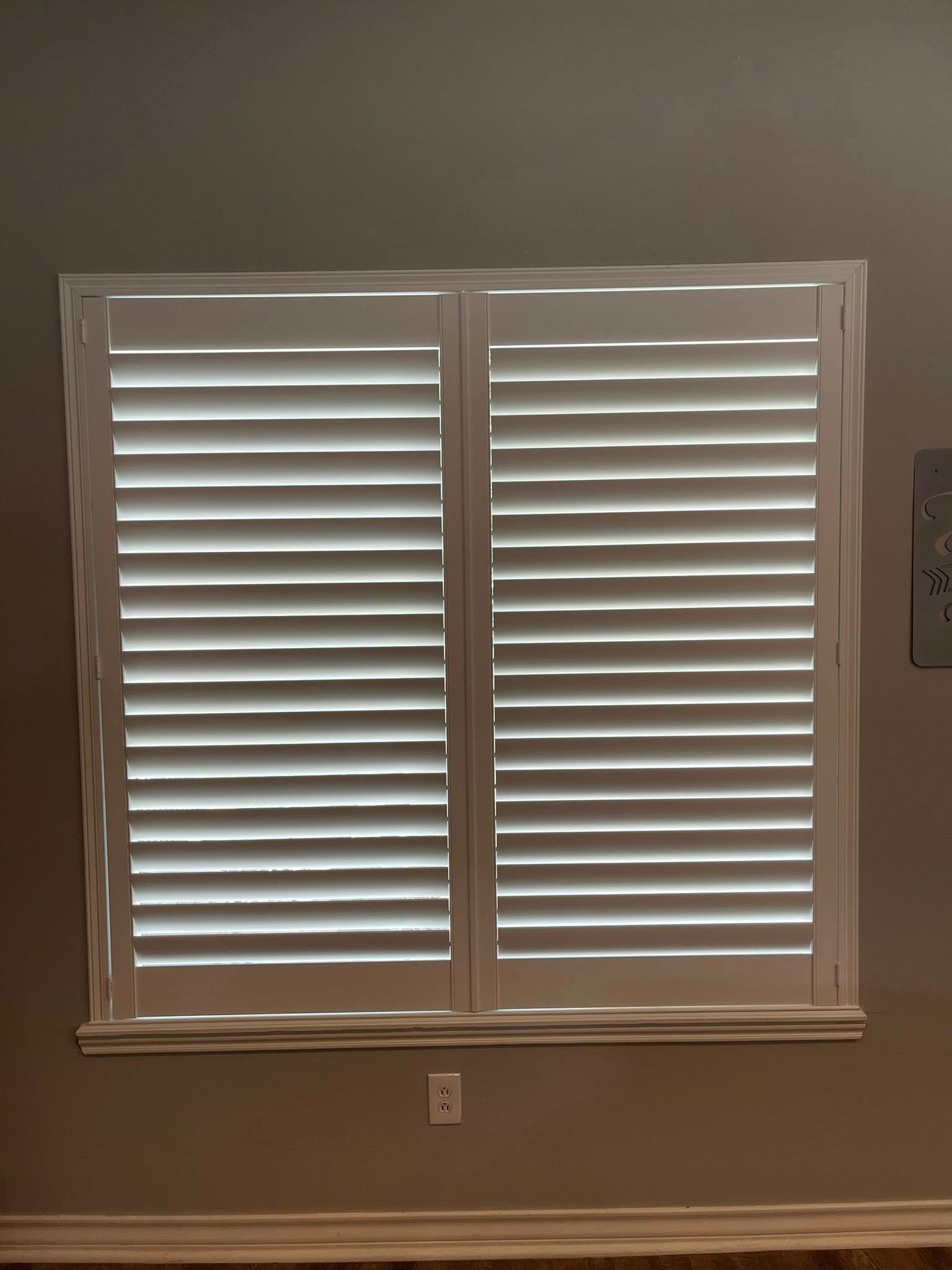 A white plantation shutter covering a rectangular window against a plain wall.