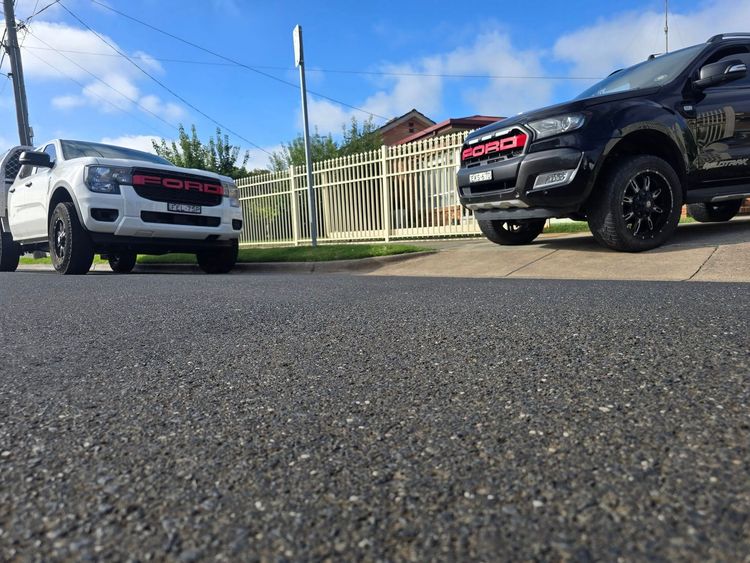 Two ford trucks are parked on the side of the road.