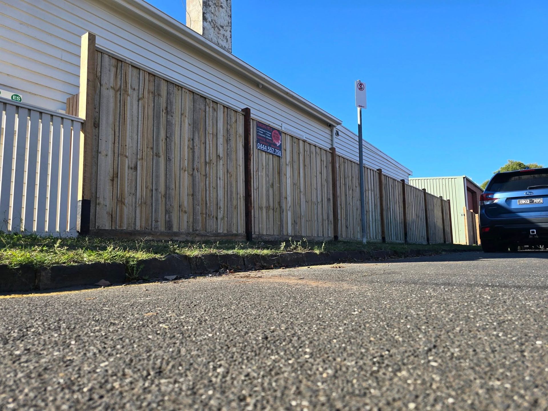 A car is parked on the side of the road next to a wooden fence.