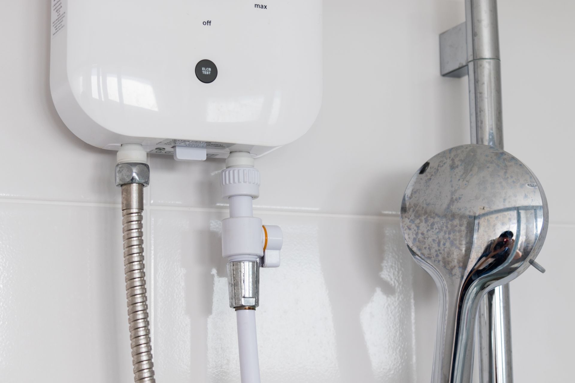 White water heater above a chrome shower hose and handheld showerhead in a tiled bathroom.