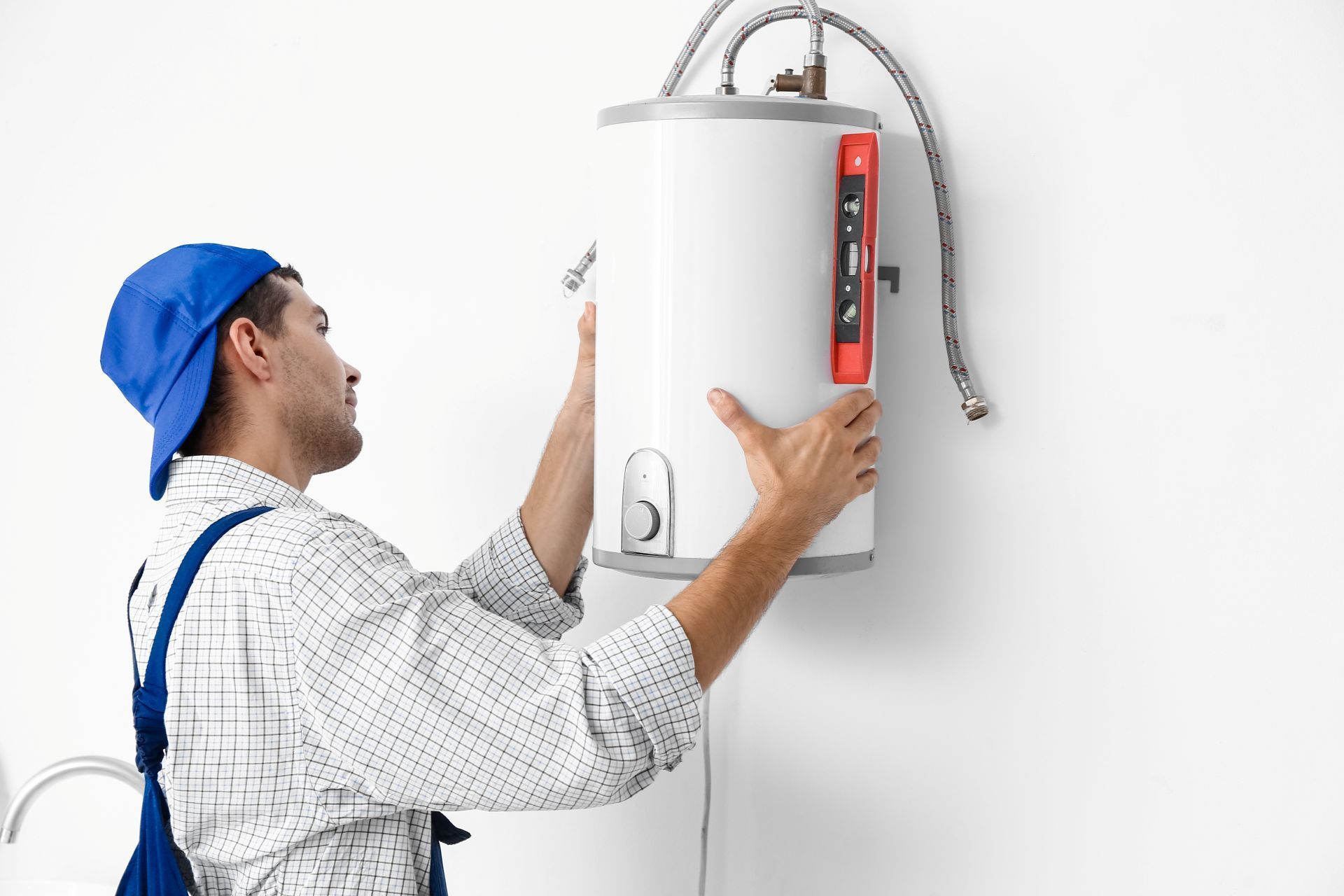 Plumber installing a white water heater on a wall, using a level to align it.