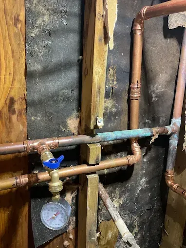 Copper pipes and a water meter beside a wall with black insulation and exposed framing.