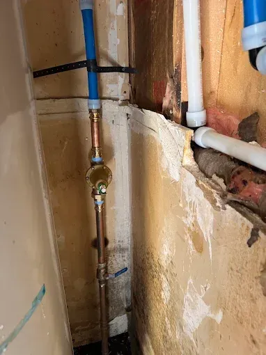 Exposed plumbing pipes and water valve inside a damaged wall cavity with peeling plaster