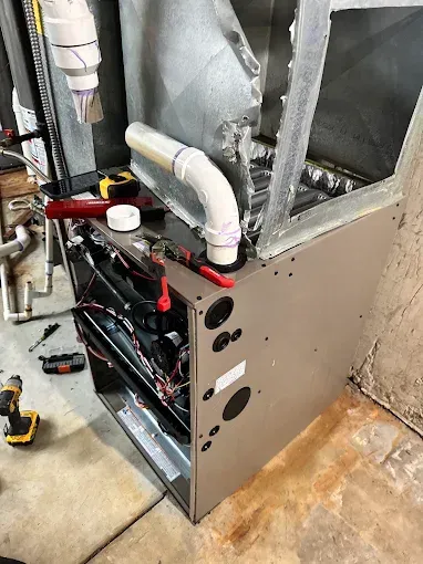 Open HVAC unit with exposed wiring, pipes, and ductwork in a basement or utility area.
