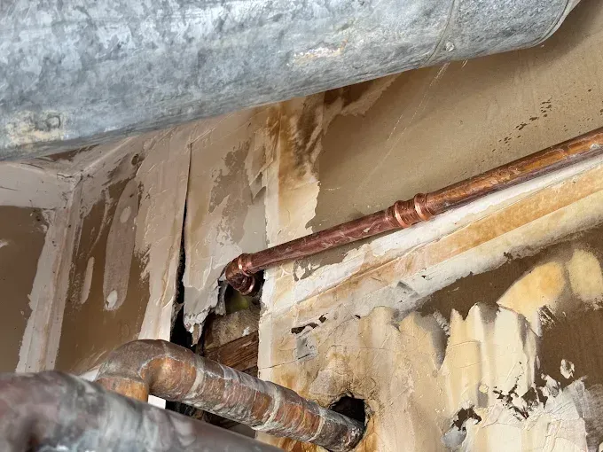 Exposed copper pipes with water damage and peeling drywall in a ceiling corner