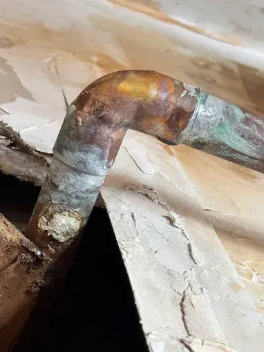 Rusty metal pipe elbow under a damaged ceiling with cracked plaster