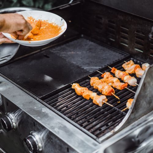 A person is cooking shrimp on skewers on a grill.