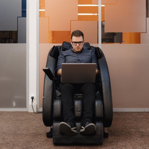 A man is sitting in a massage chair using a laptop
