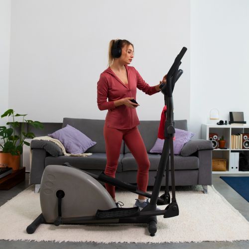 A woman is standing next to an elliptical machine in a living room.