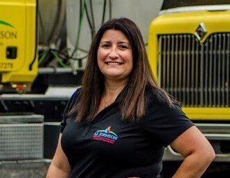 A woman in a black shirt is standing in front of a yellow truck.