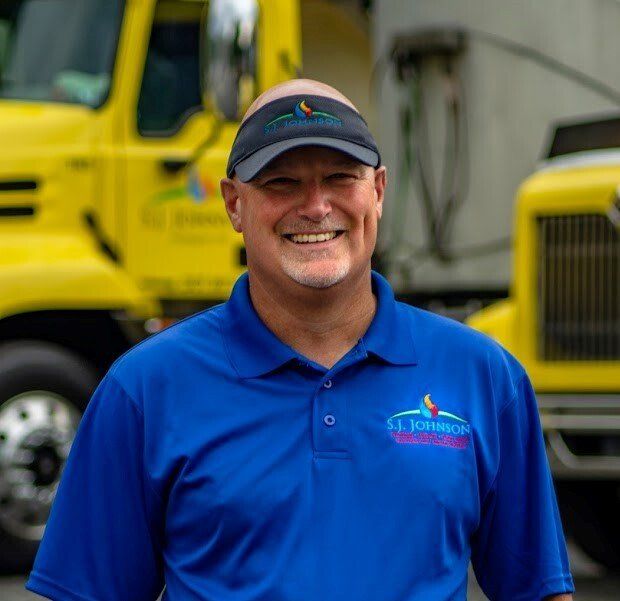 A man in a blue shirt is smiling in front of a yellow truck